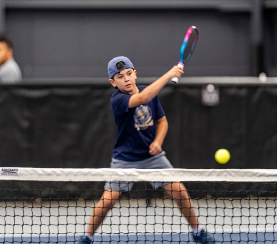 A Junior Academy player in a Greystone shirt hits a backhand at the net
