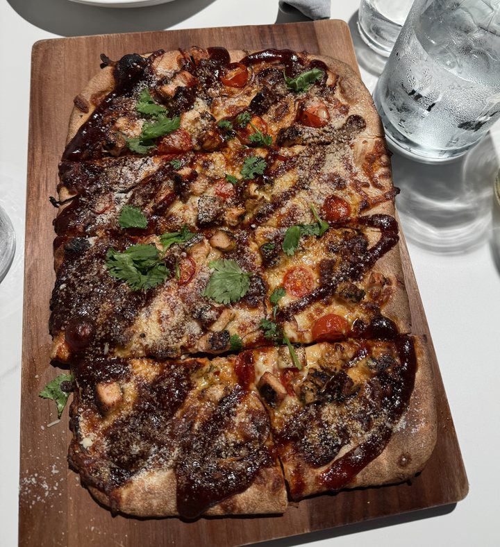 A BBQ chicken flatbread with cherry tomatoes and cilantro on a wood board