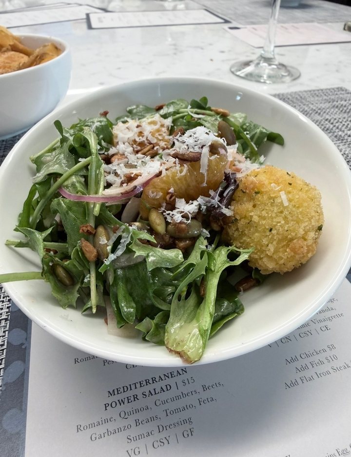 A green salad with orange segments, pepitas, shaved parmesan and a fried goat cheese ball