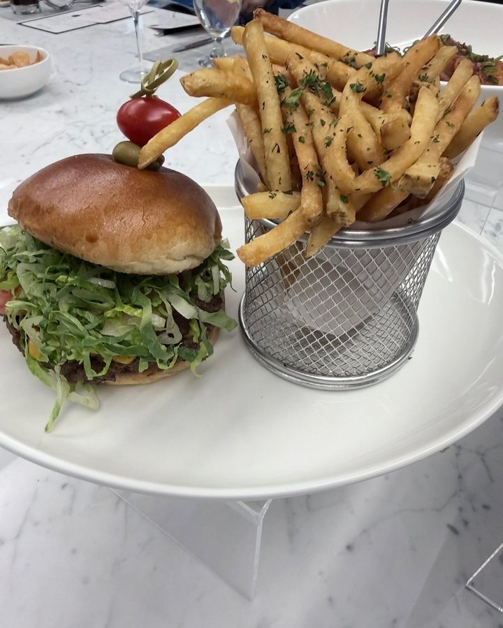 A burger with shredded lettuce on a brioche bun, served with herb fries in a wire basket