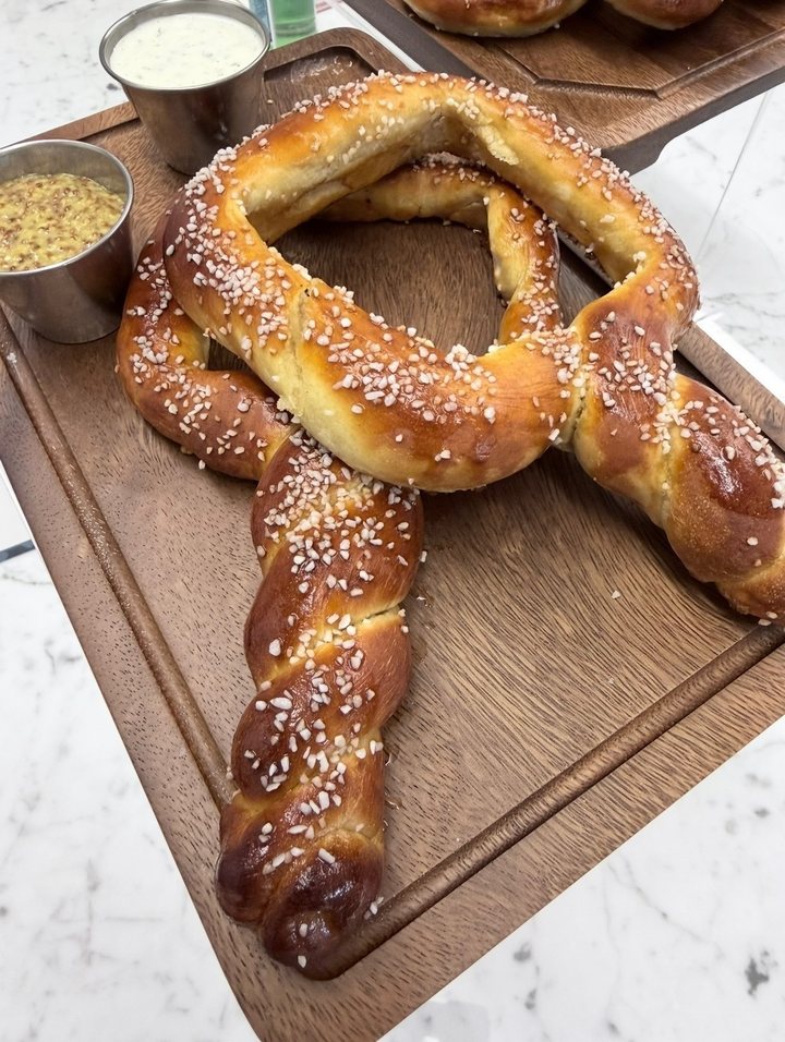 A giant soft pretzel with coarse salt, served on a wood board with beer cheese and grain mustard