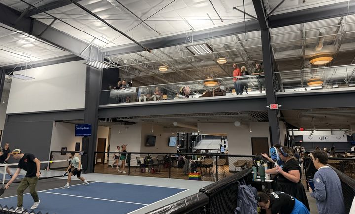 Open play at Greystone: players rallying at the net on a court while members watch from the mezzanine above