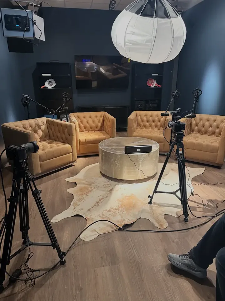 The podcast studio at Greystone: four leather armchairs around a round table, cameras on tripods, microphones, and a softbox light