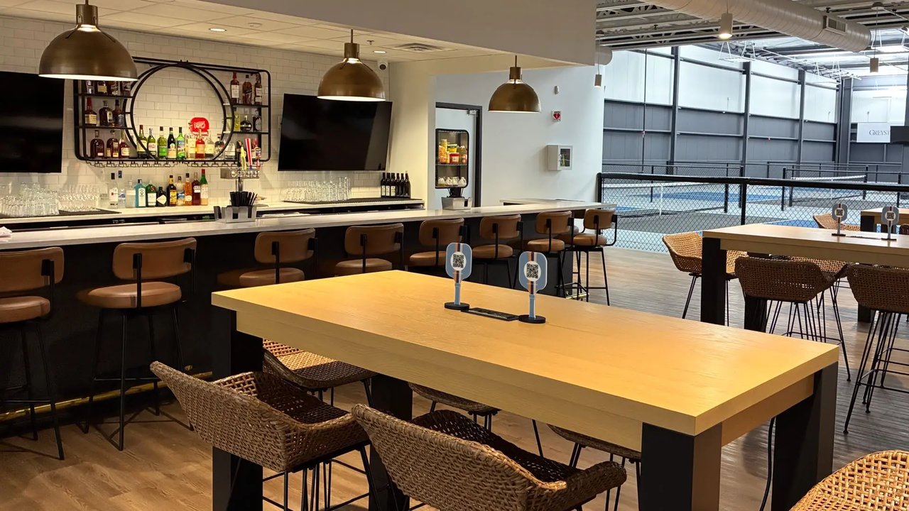 The Greystone Grill bar with pendant lights, bottles on the back shelf, and the courts visible through the glass