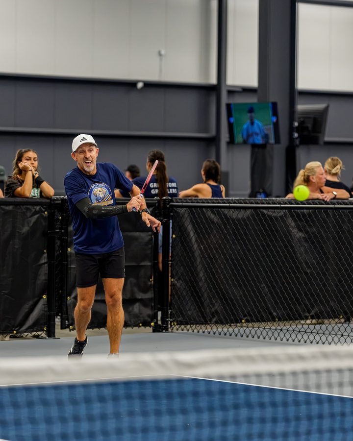 A player laughs at the court rail while friends watch from behind the fence